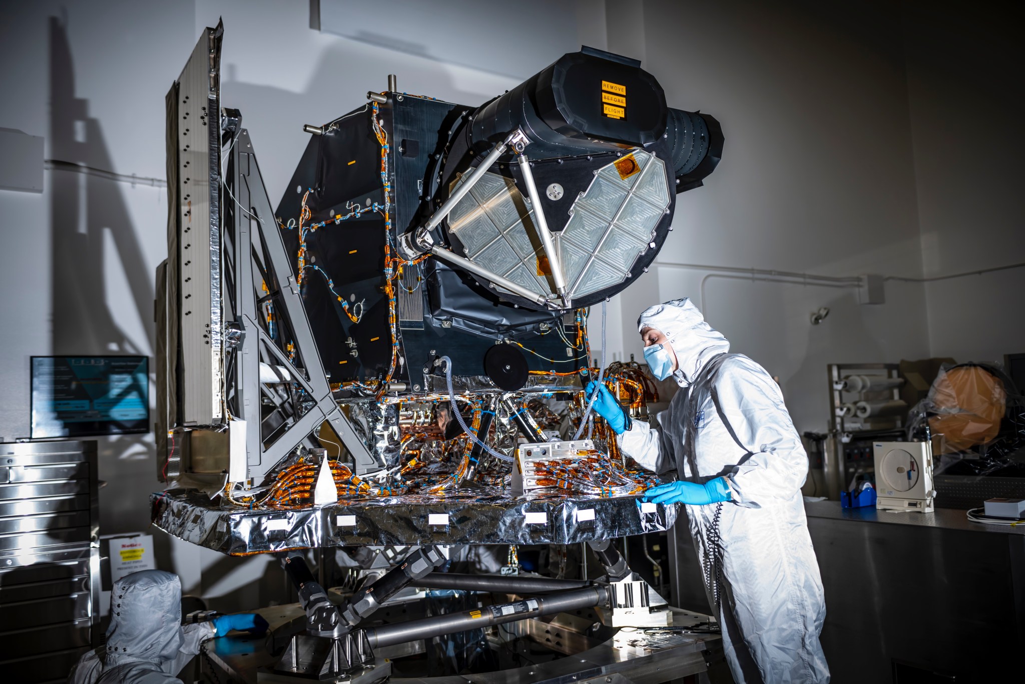 The Operational Land Imager 2 instrument in a clean room, being inspected by someone in a white clean room suit with blue gloves and a mask.