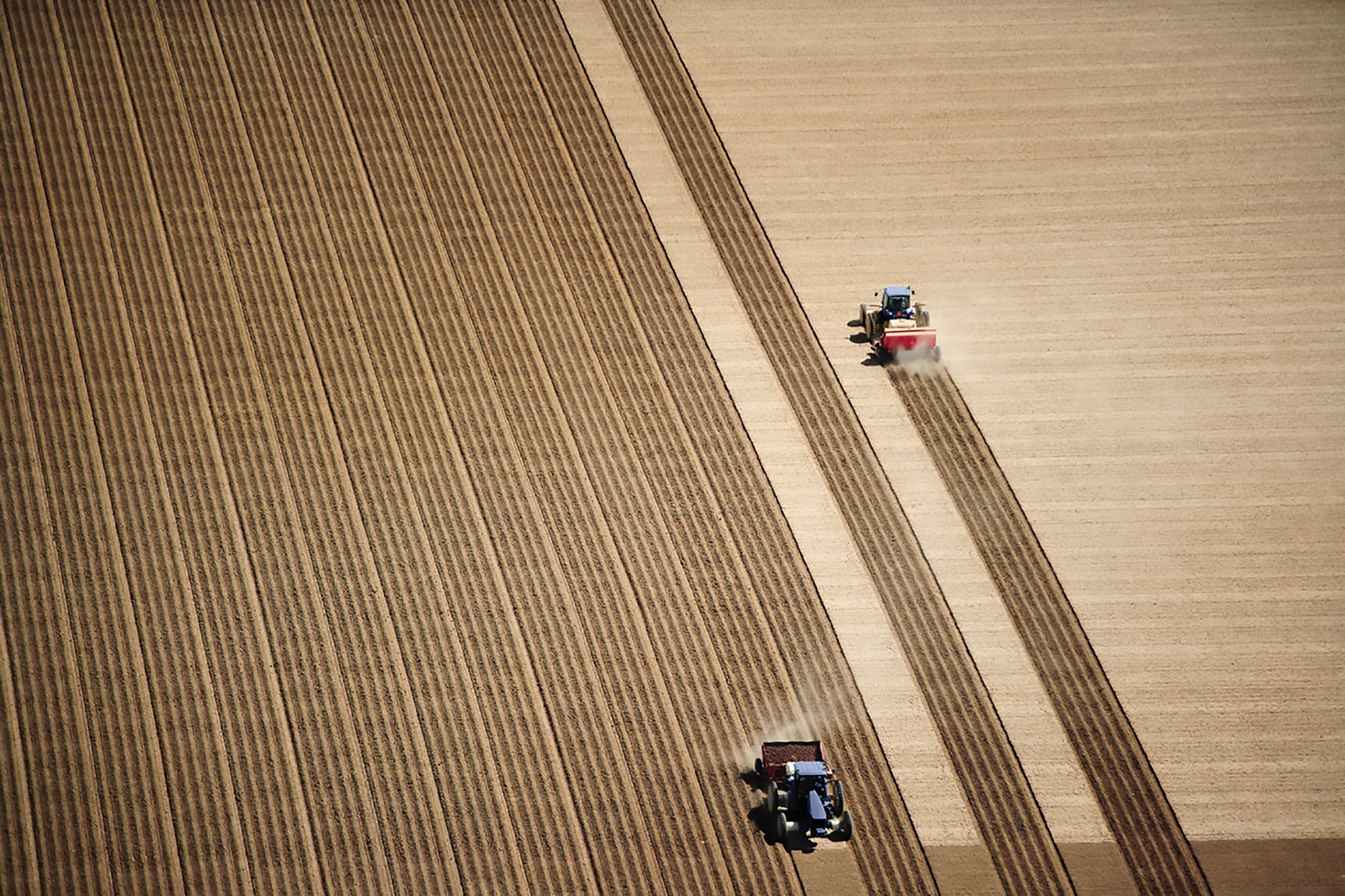 Farmers drive tractors in a large field.