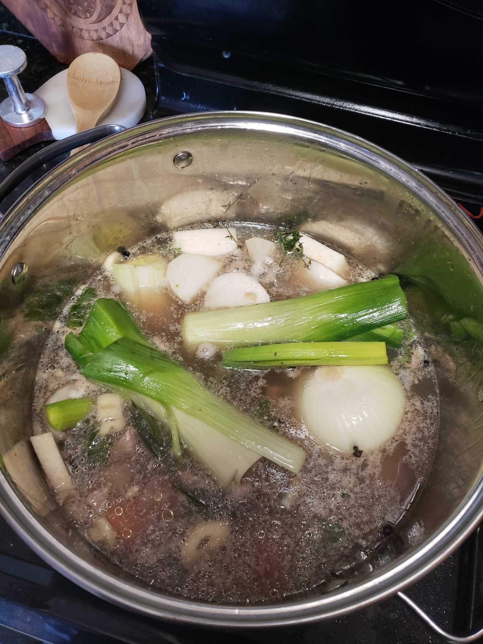 French stew on a pot on a stove, leeks, potatoes, celery root, and onion are visible in broth