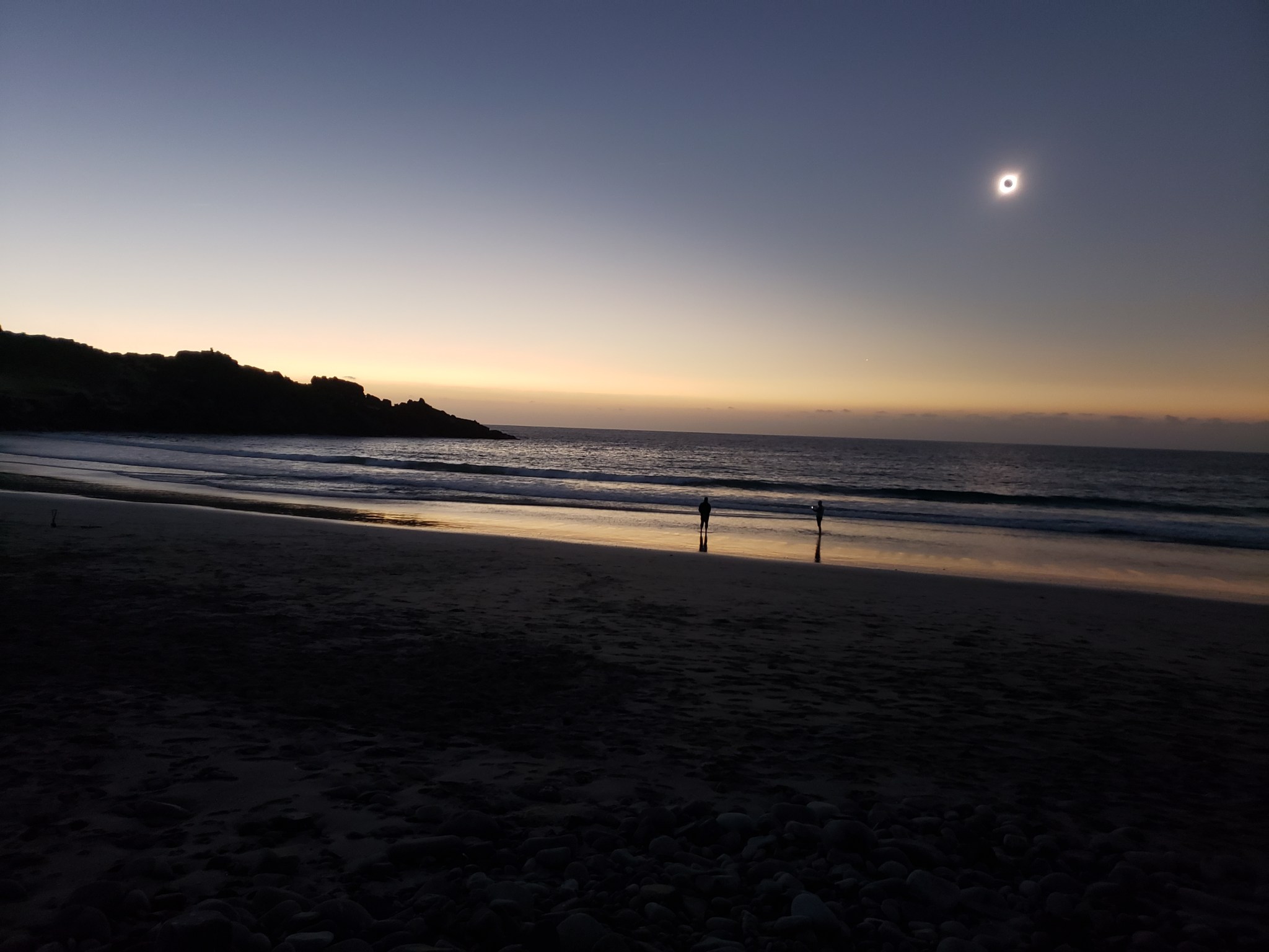 photo of an eclipse on a beach in Chile, there are two silhouettes of people on the beach