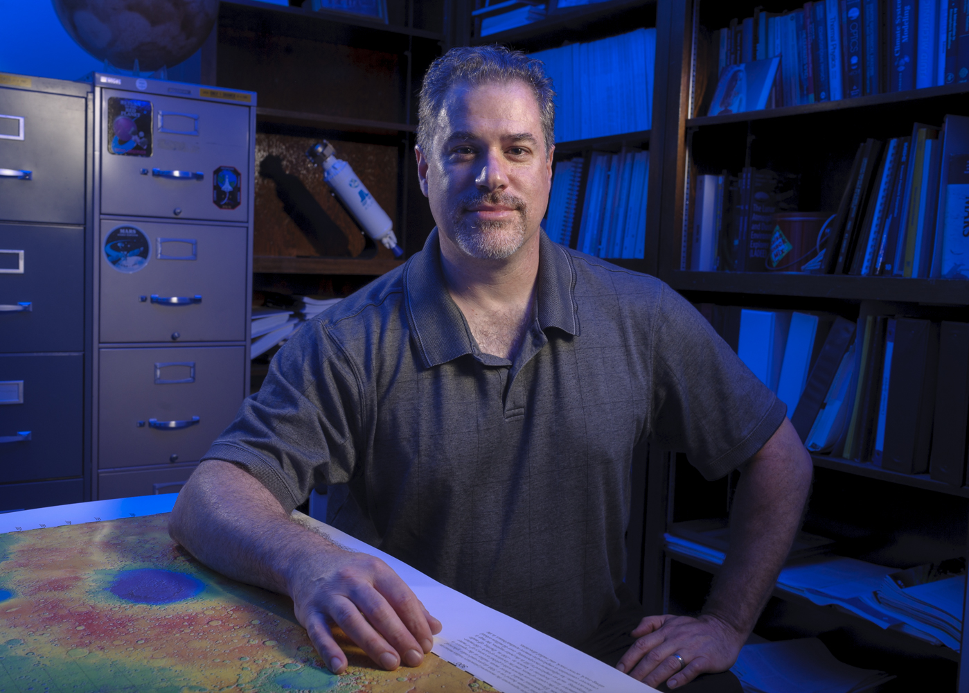 NASA scientist Tony Colaprete in his office with a model of the LCROSS spacecraft behind him.