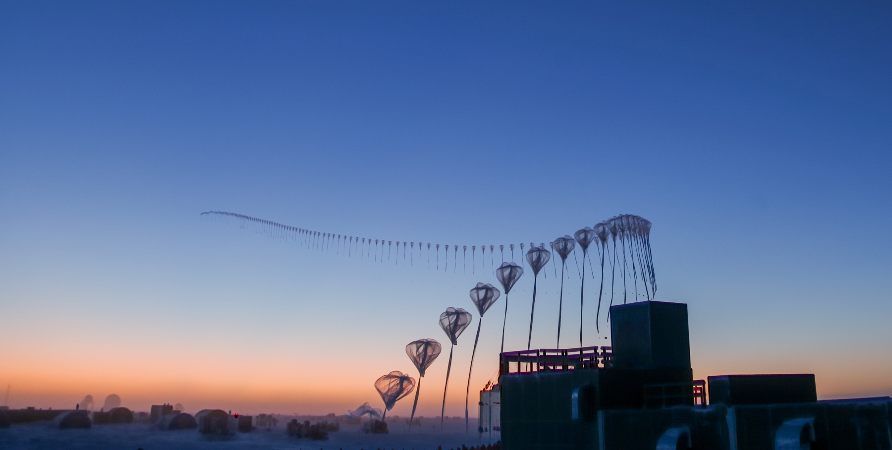 Timelapse photo of a weather balloon launching, with each step of the balloon's inflation and early flight as one step. The balloons create a long curved line from the ground out into space.