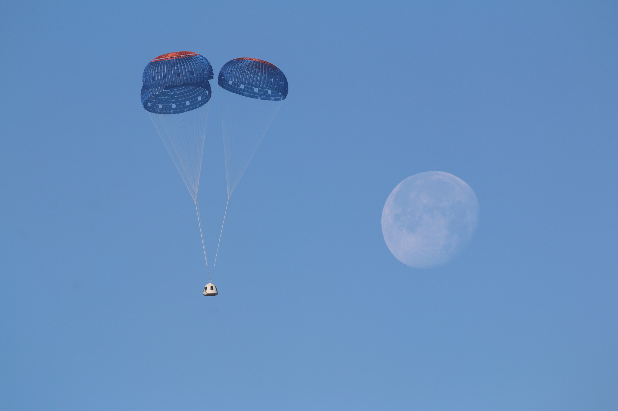 Payload attached to two balloons with a blue sky background and a faded, daytime view of the Moon