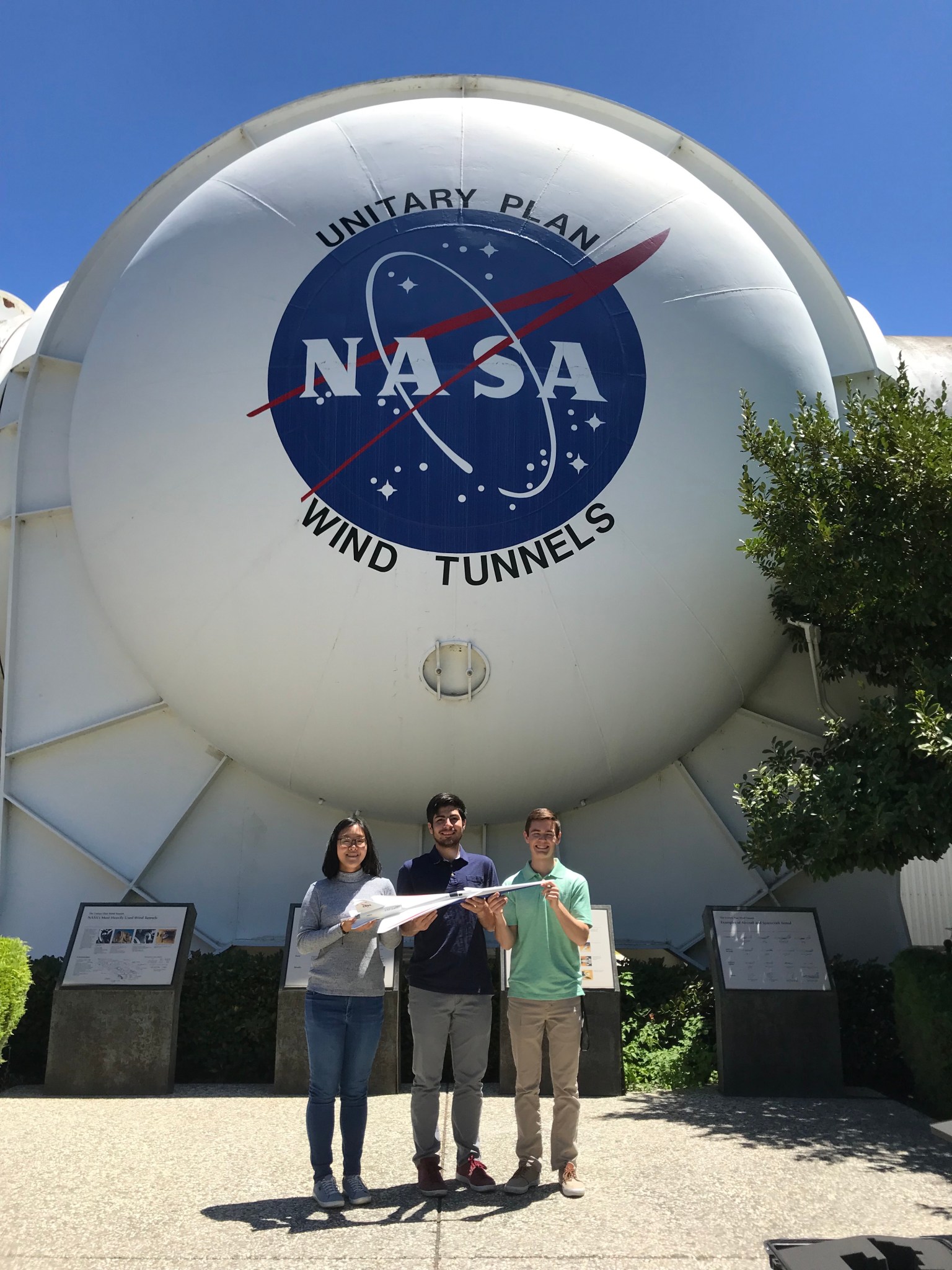 NASA interns hold a model of the X-59 standing outside the Unitary Plan Wind Tunnel.