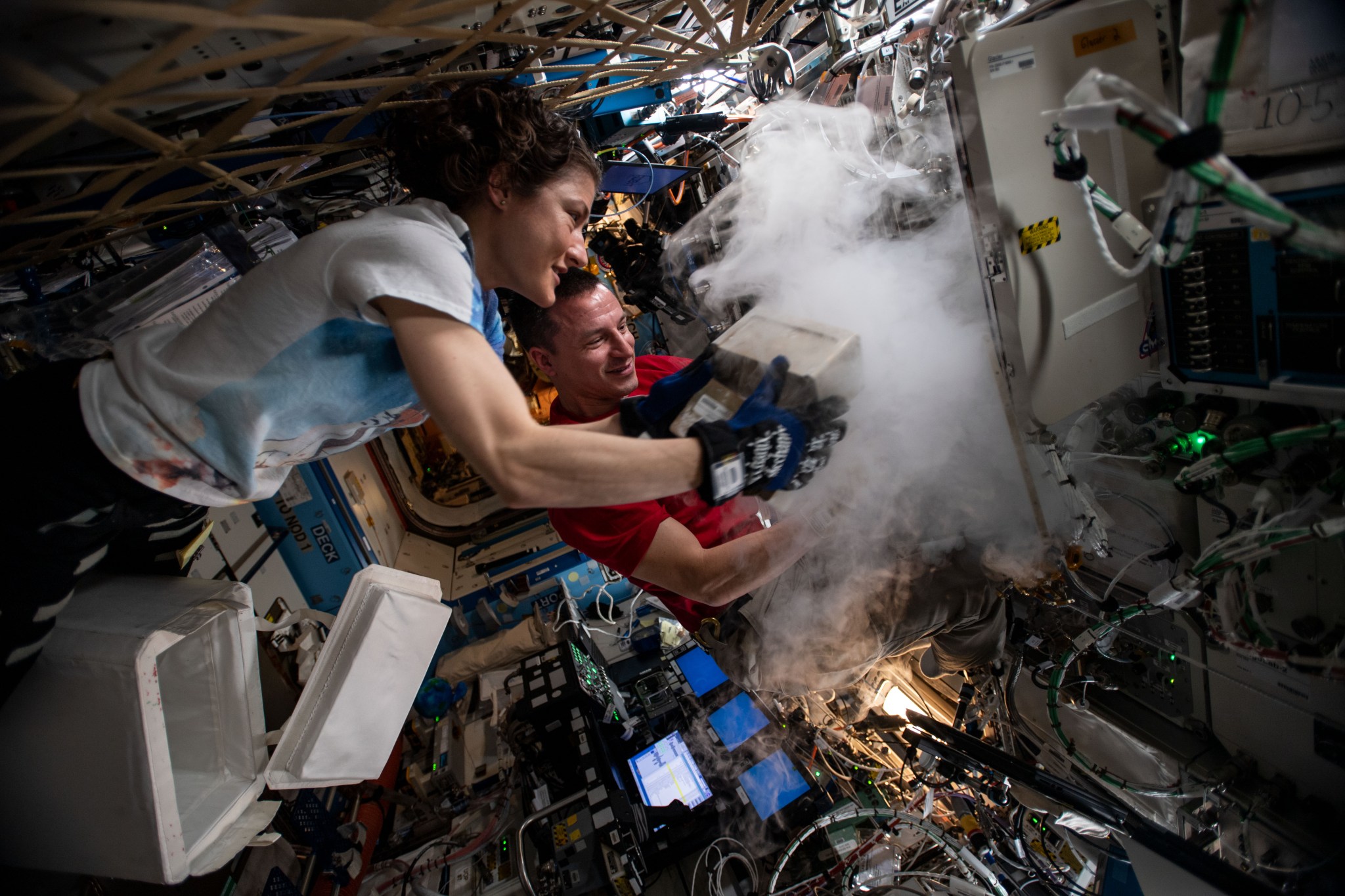 NASA astronauts Christina Koch and Andrew Morgan stow biological research samples into a science freezer located inside the ISS