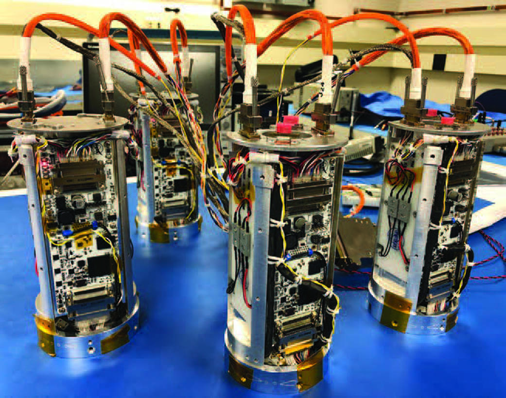 four small cylinder payloads with many wires on a blue tabletop.