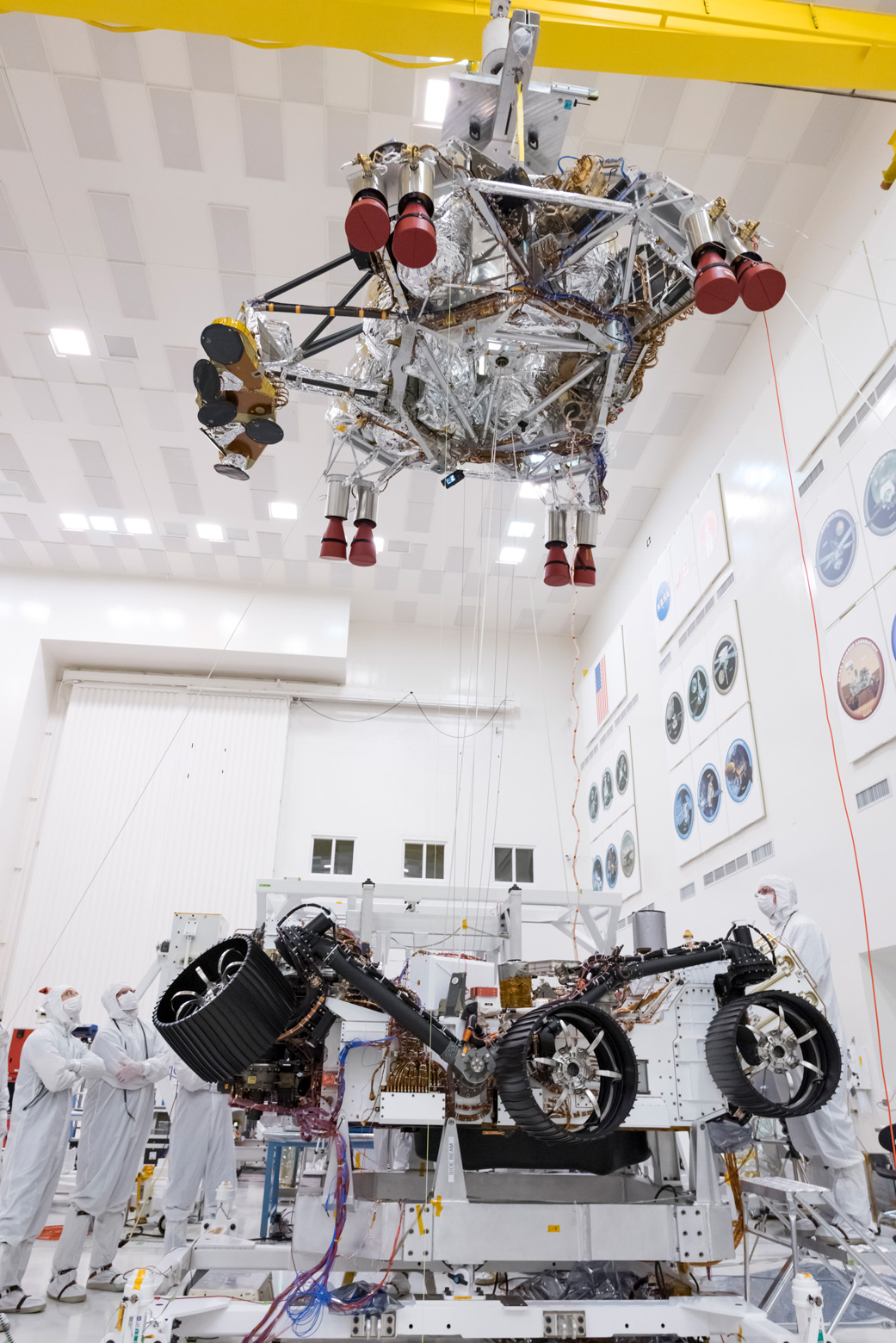 Employees look on as a crane lifts the rocket-powered descent stage away from the Mars 2020 rover