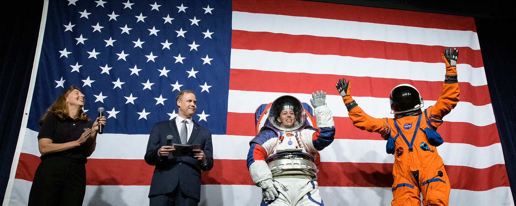 Four people in front of American flag, 2 in space suits