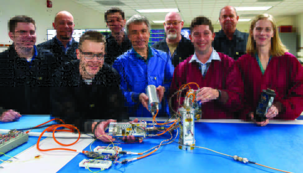 Photo of 8 men and one woman holding technology with many wires.