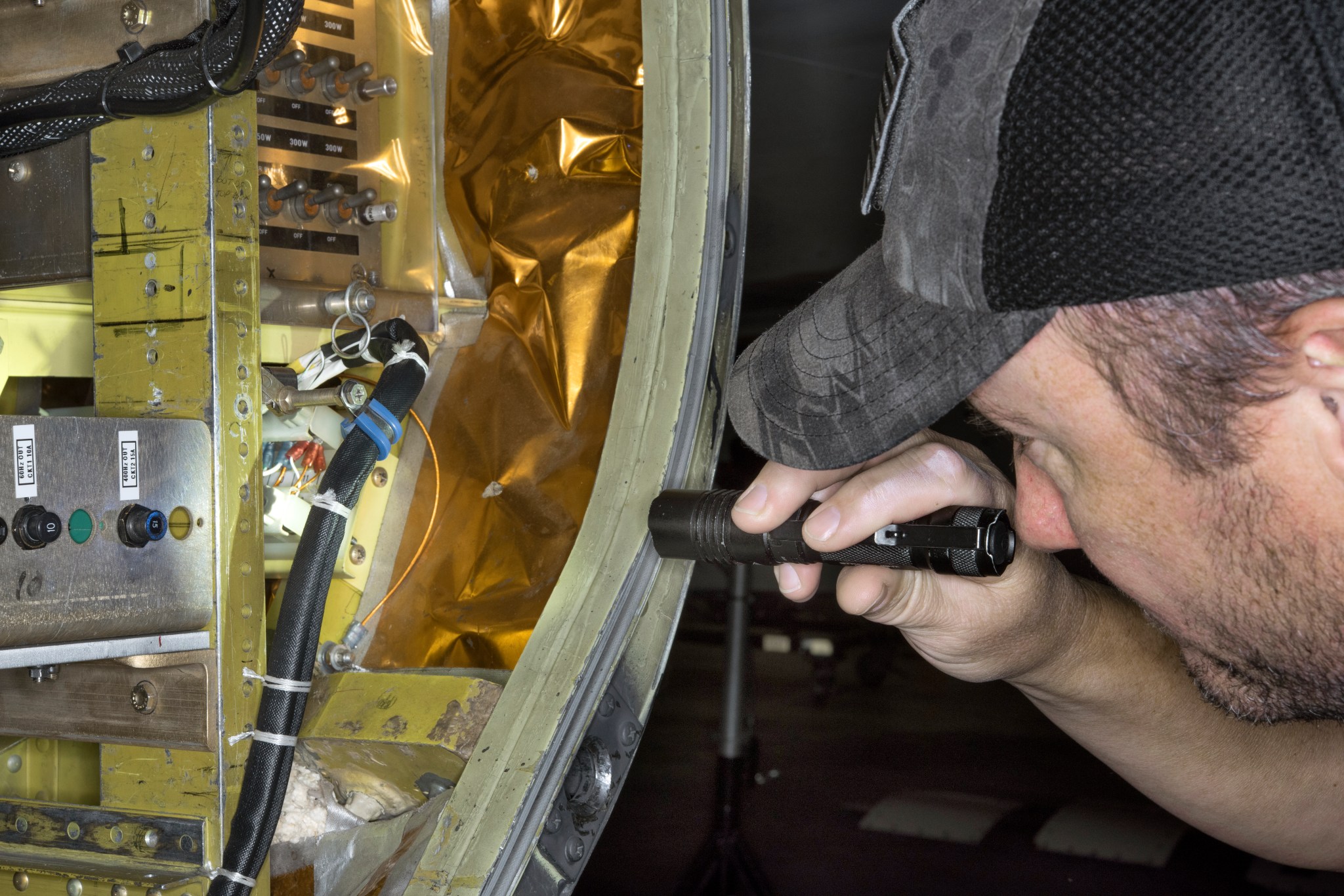 A crew member uses a small flashlight to inspect instrumentation.
