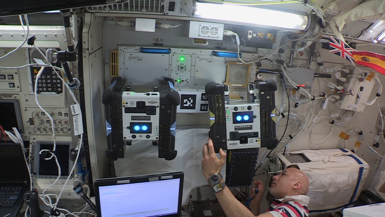European Space Agency astronaut Luca Parmitano places the second Astrobee robot, named Honey, on Astrobees docking station in t
