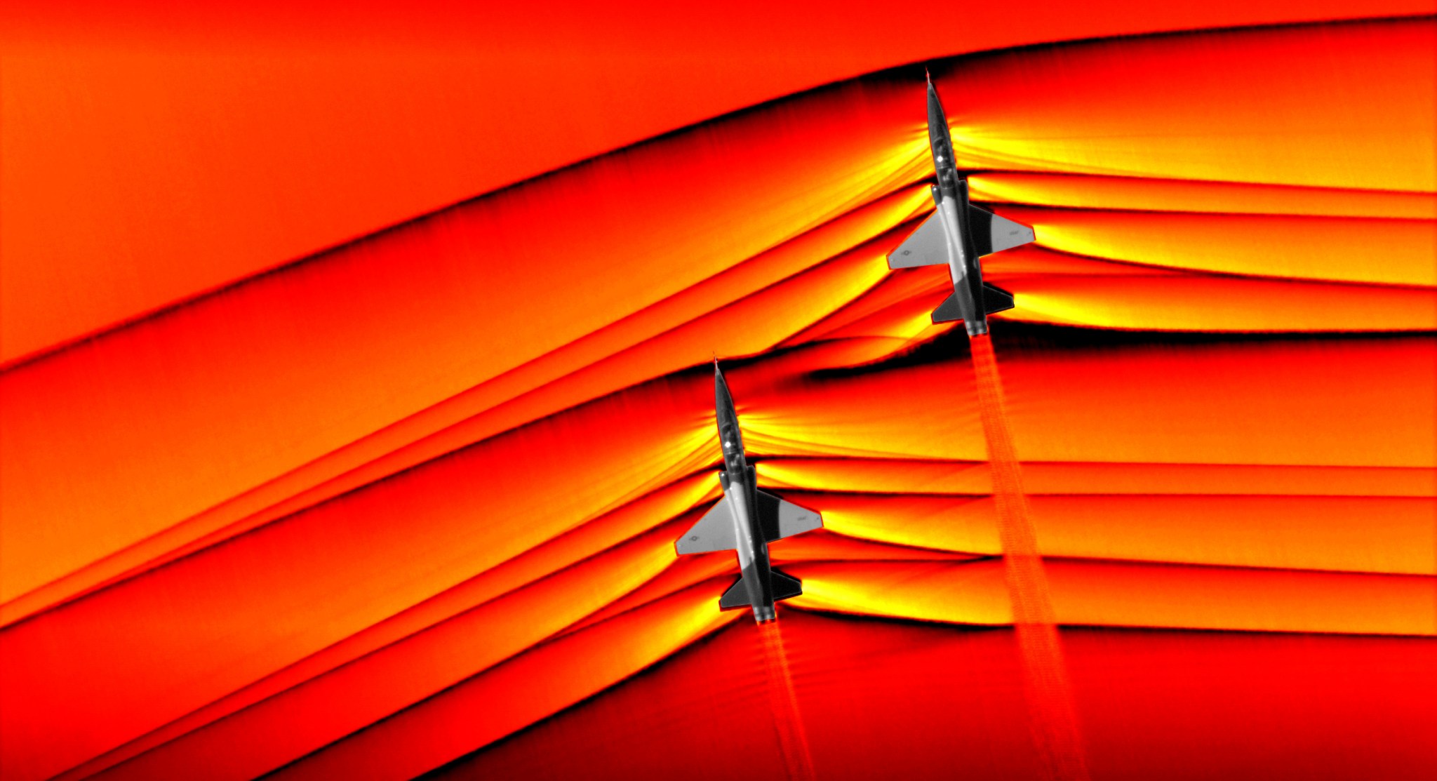 Two U.S. Air Force Test Pilot School T-38 aircraft flying in formation at supersonic speed.