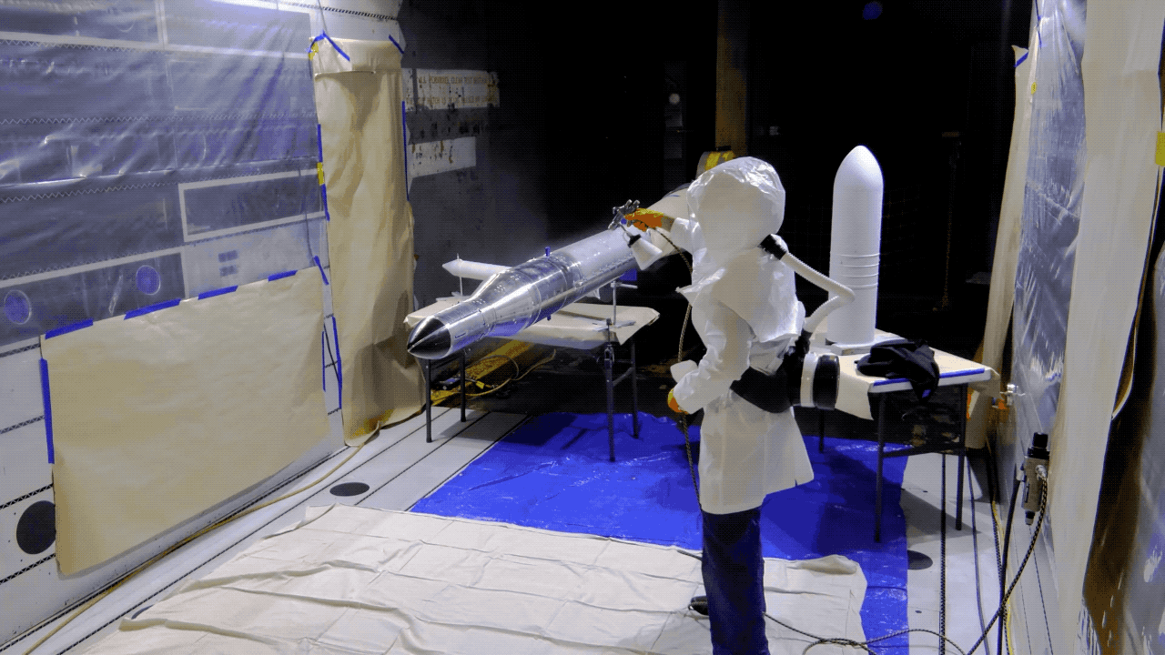 Timelapse of two people wearing protective gear spraypainting a rocket model