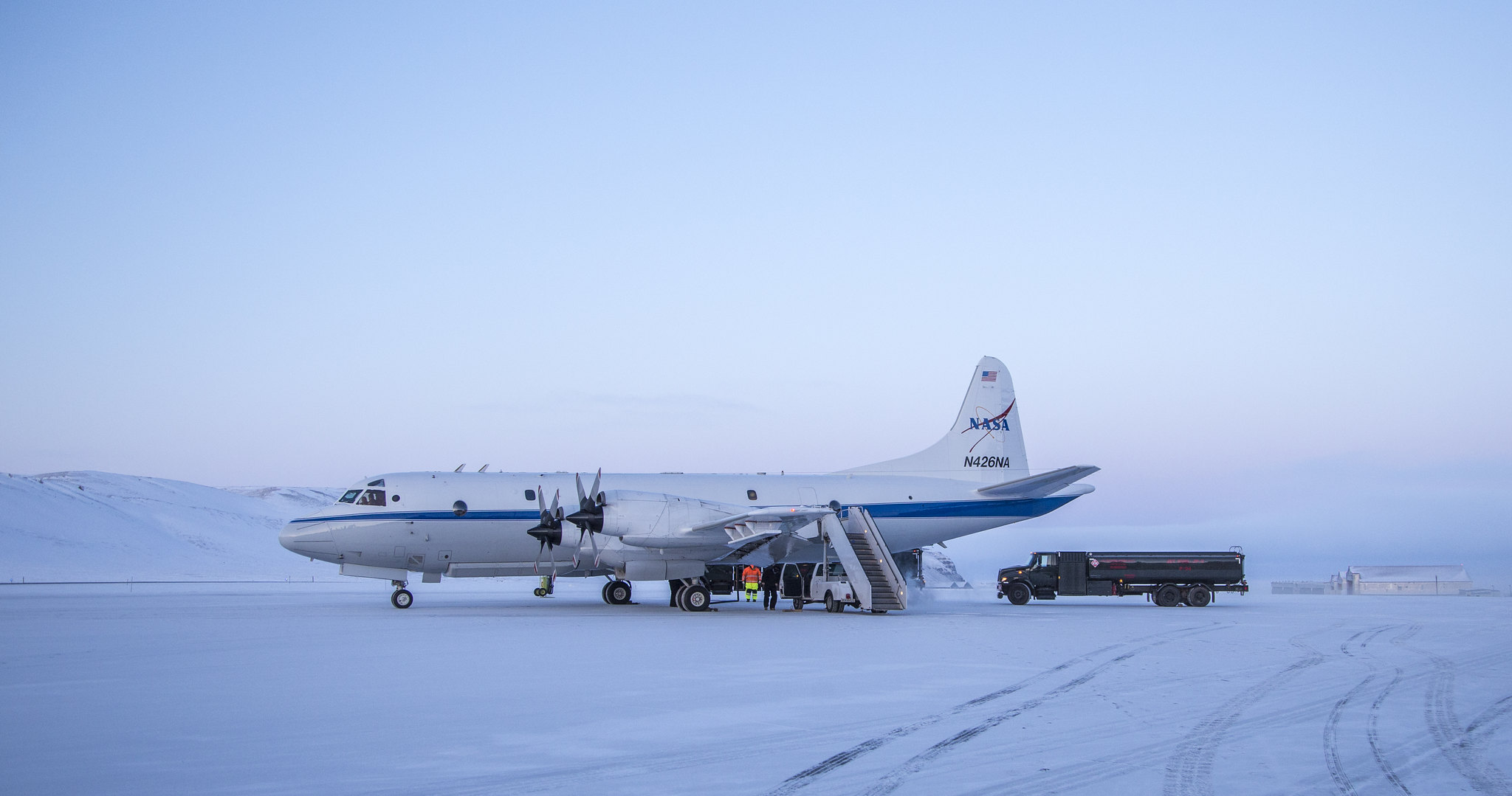 The P-3 aircraft, a white plane with blue strip down the side, sits on an snow-covered landscape.