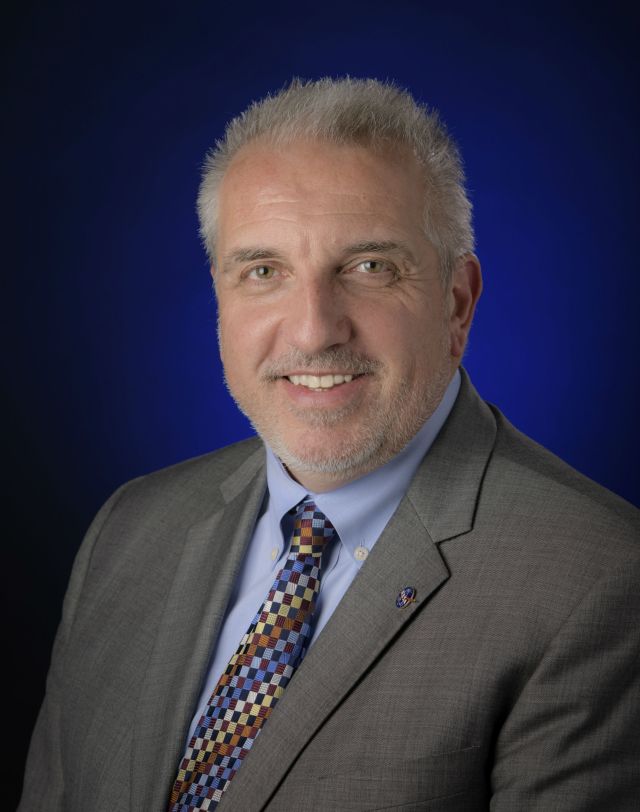 Bob Pearce wearing a tan suite and a colorful checkered tie.