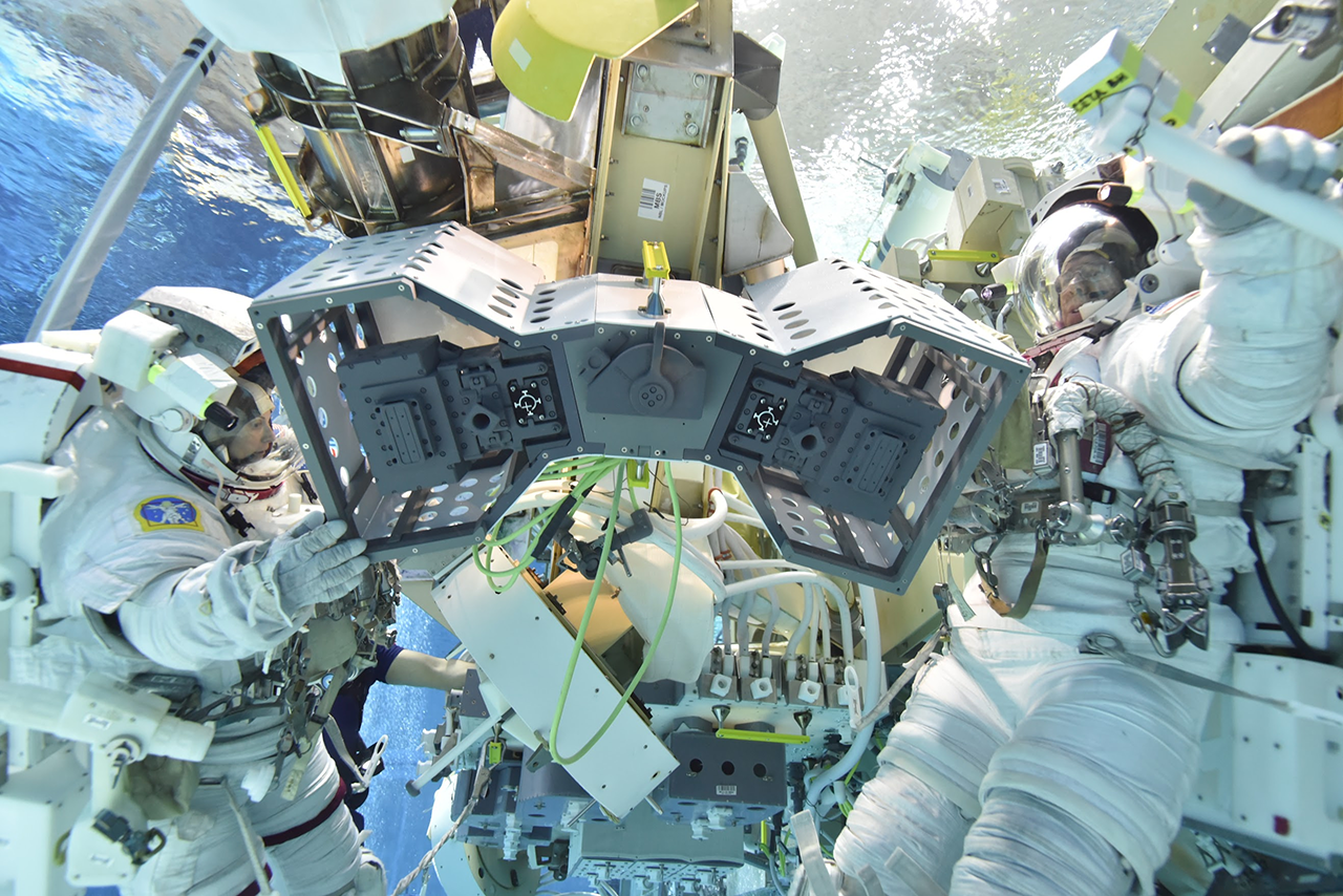 RiTS spacewalk install procedures being tested in the Neutral Buoyancy Lab. People in astronauts suits work on a mechanical structure under water in a pool.