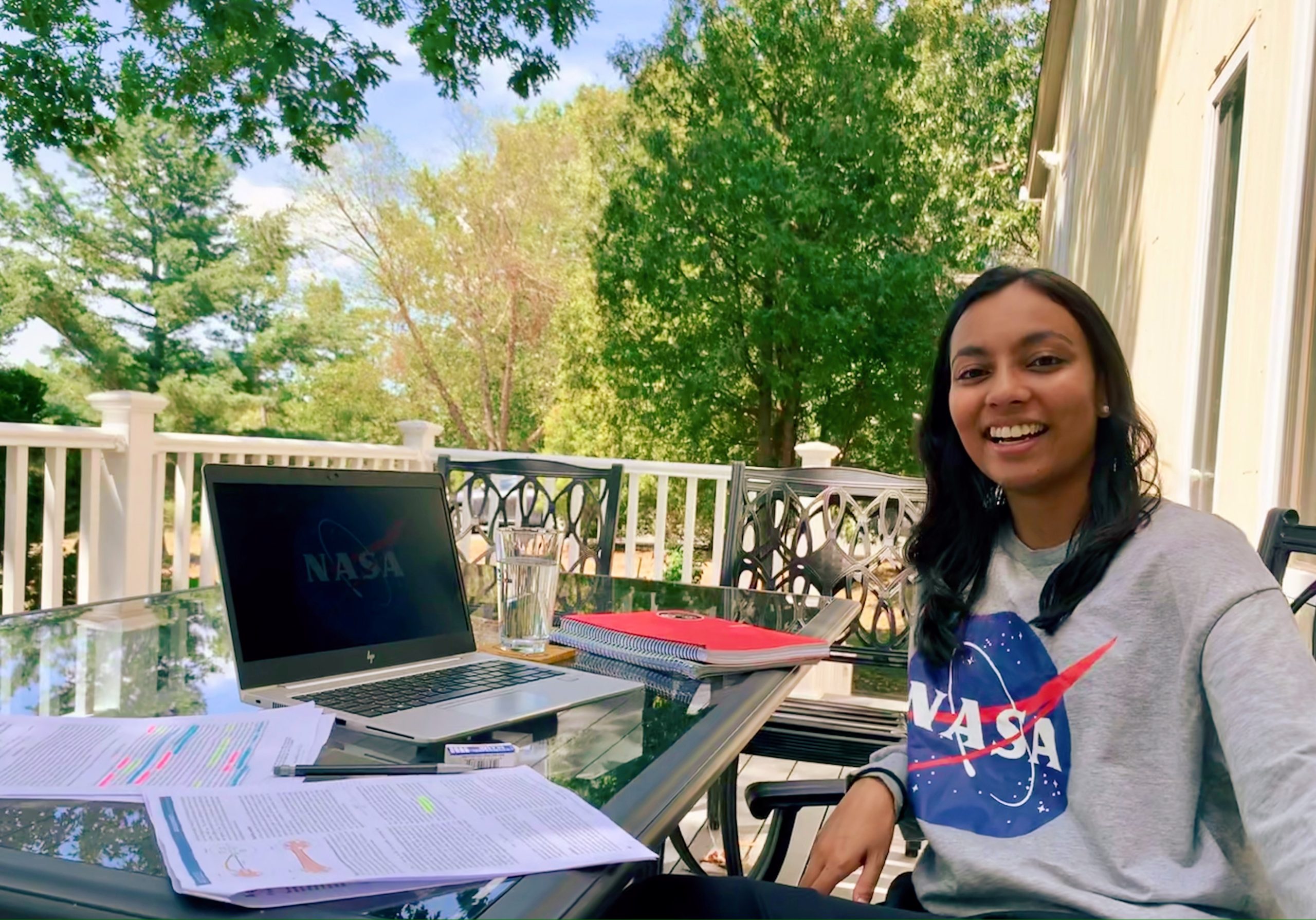An intern sits next to an open laptop at a patio table.