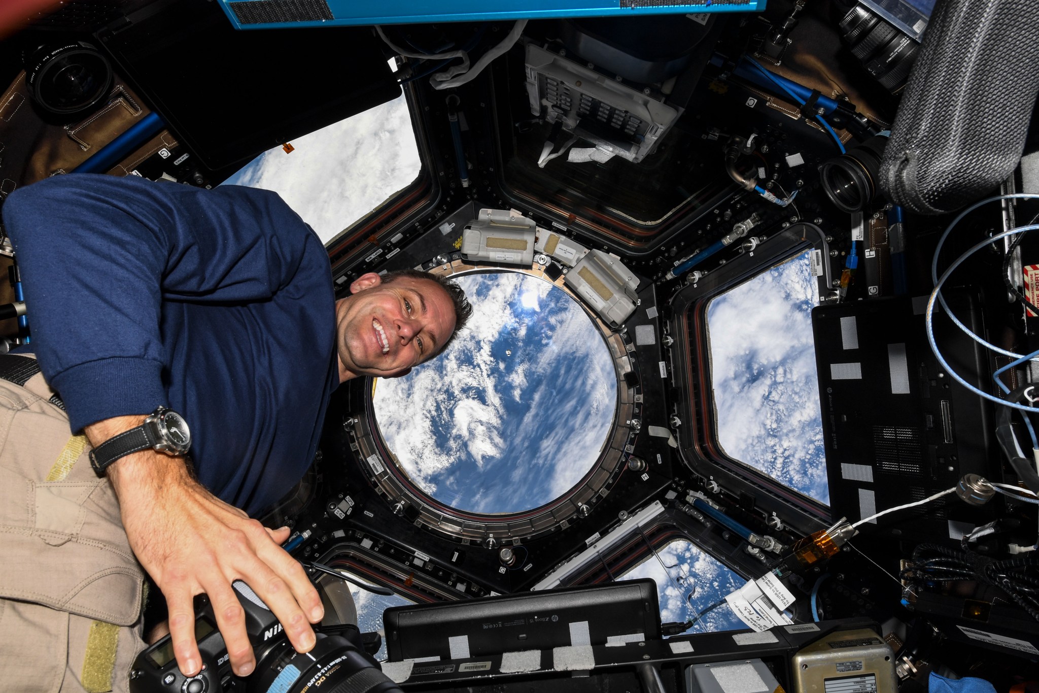image of an astronaut taking photos inside the cupola of the space station with views of Earth in backdrop
