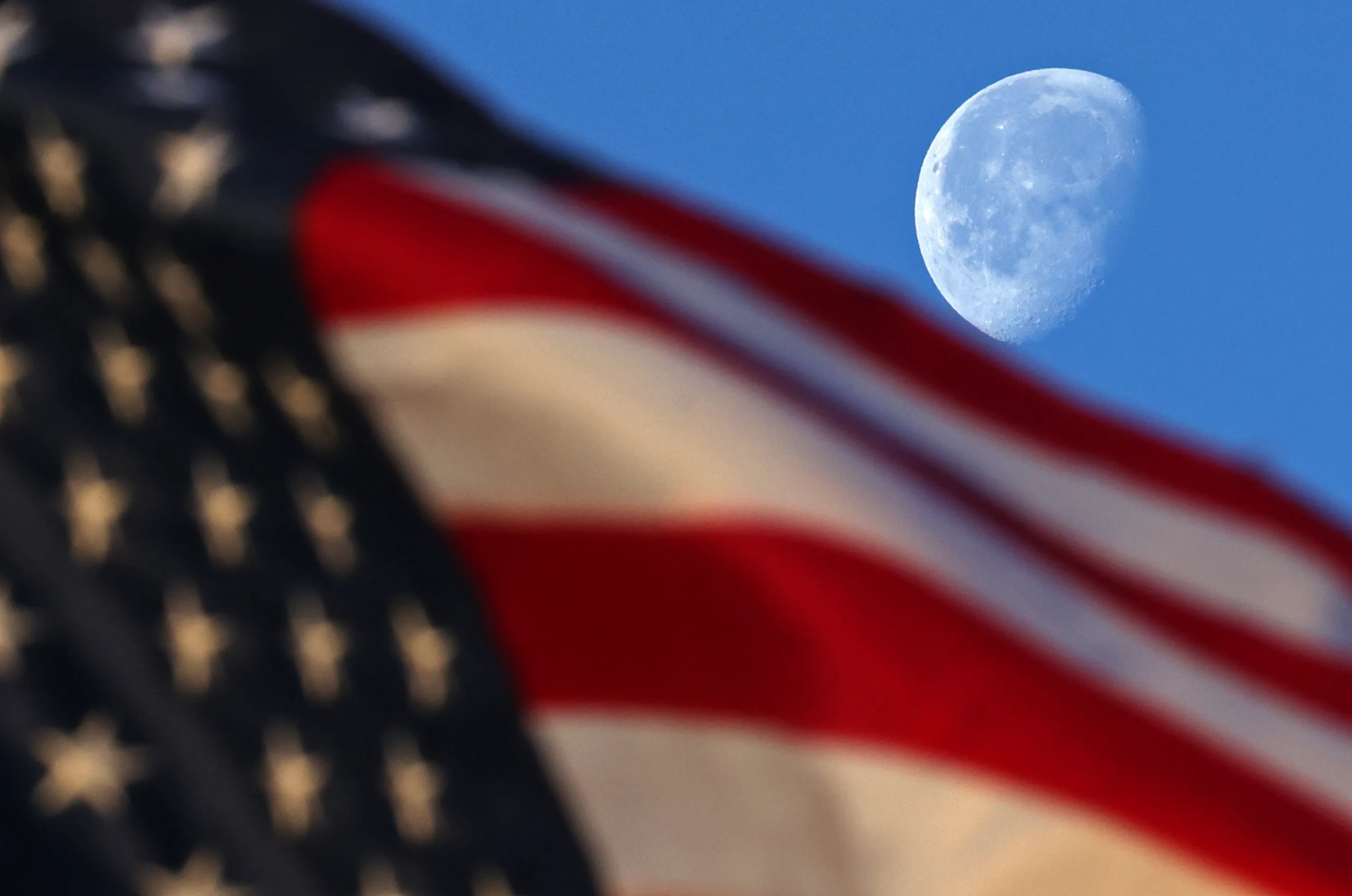 Just after sunrise, the waning gibbous moon sets just behind a waving United States flag on March 19, 2025, in this image from NASA’s Michoud Assembly Facility in New Orleans. The waning gibbous moon phase comes after the full moon. As the Moon begins its journey back toward the Sun, the opposite side of the Moon now reflects the Moon’s light. The lighted side appears to shrink, but the Moon’s orbit is simply carrying it out of view from our perspective. The Moon also rises later and later each night.