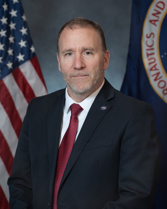 Portrait of Tim McCartney with U.S. and NASA flags in background.