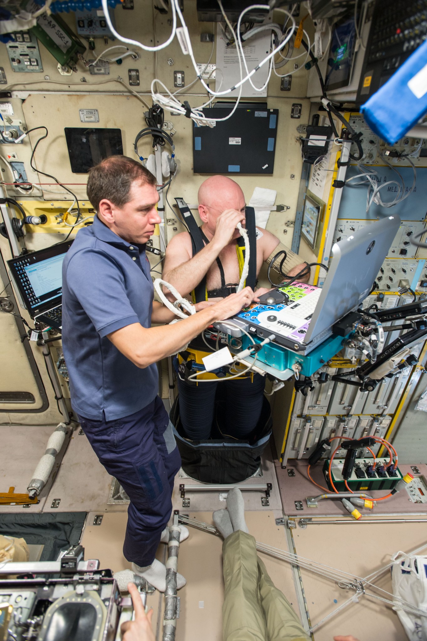 astronaut Scott Kelly strapped into ultrasound gear, which is operated by cosmonaut Sergey Volkov