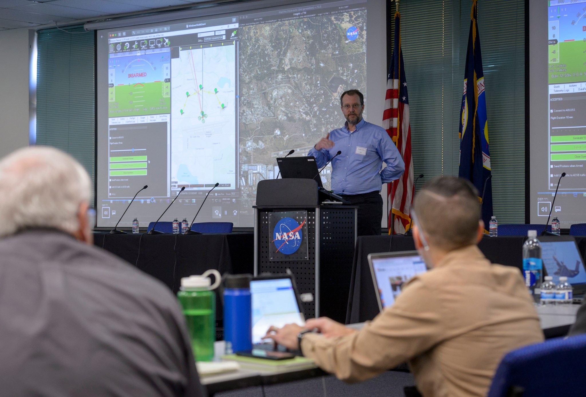A man speaks in front of a large screen showing flight-planning and drone traffic management software.