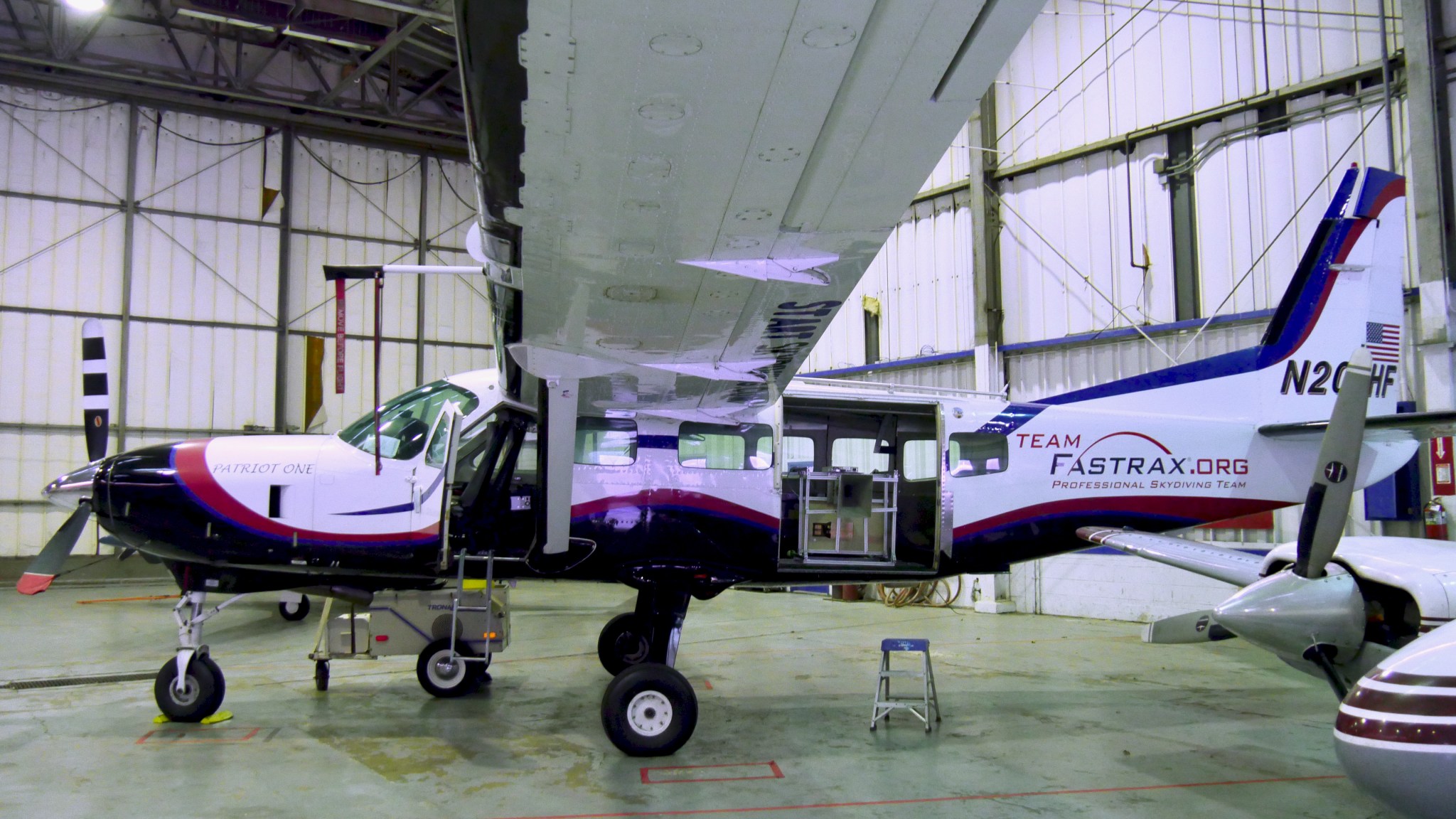  A small plane sits in a hangar with its doors open. In the back side, door, a squat, cube instrument is visible. 