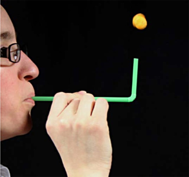 Man blows into a straw as a cheese puff floats above the other end