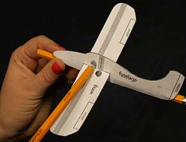 A paper model of an airplane attached to pencils that run across the wings and along the fuselage