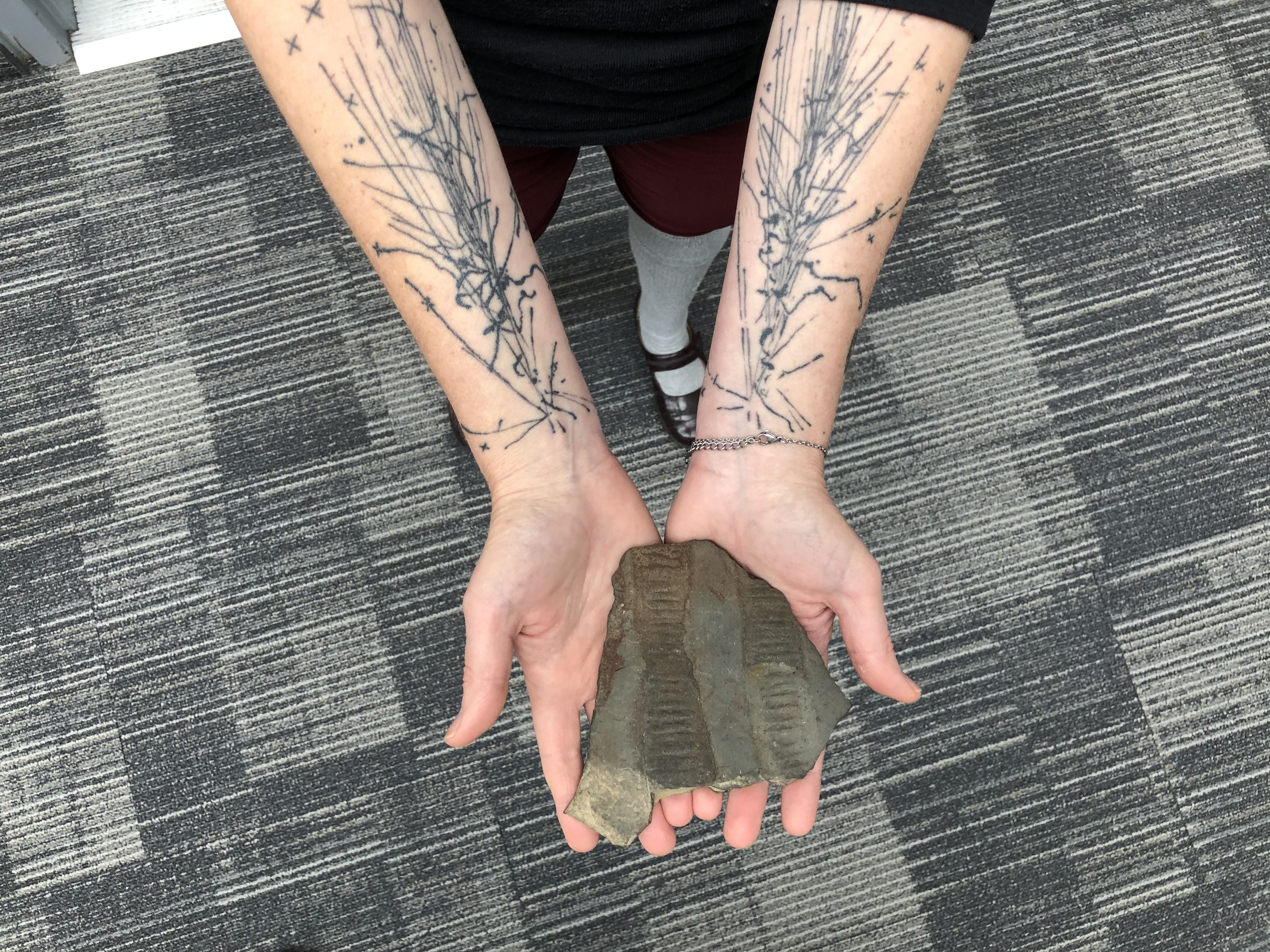 Astrobiologist Heather Graham holds a 600-million-year-old fossil. Her tattoos represent high-speed particle collisions. 