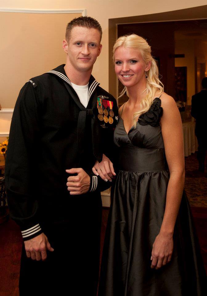 Uffner, dressed in his Navy dress uniform, a man with short brown hair, accompanied by his wife, a woman with long blonde hair, wearing a formal black dress. 