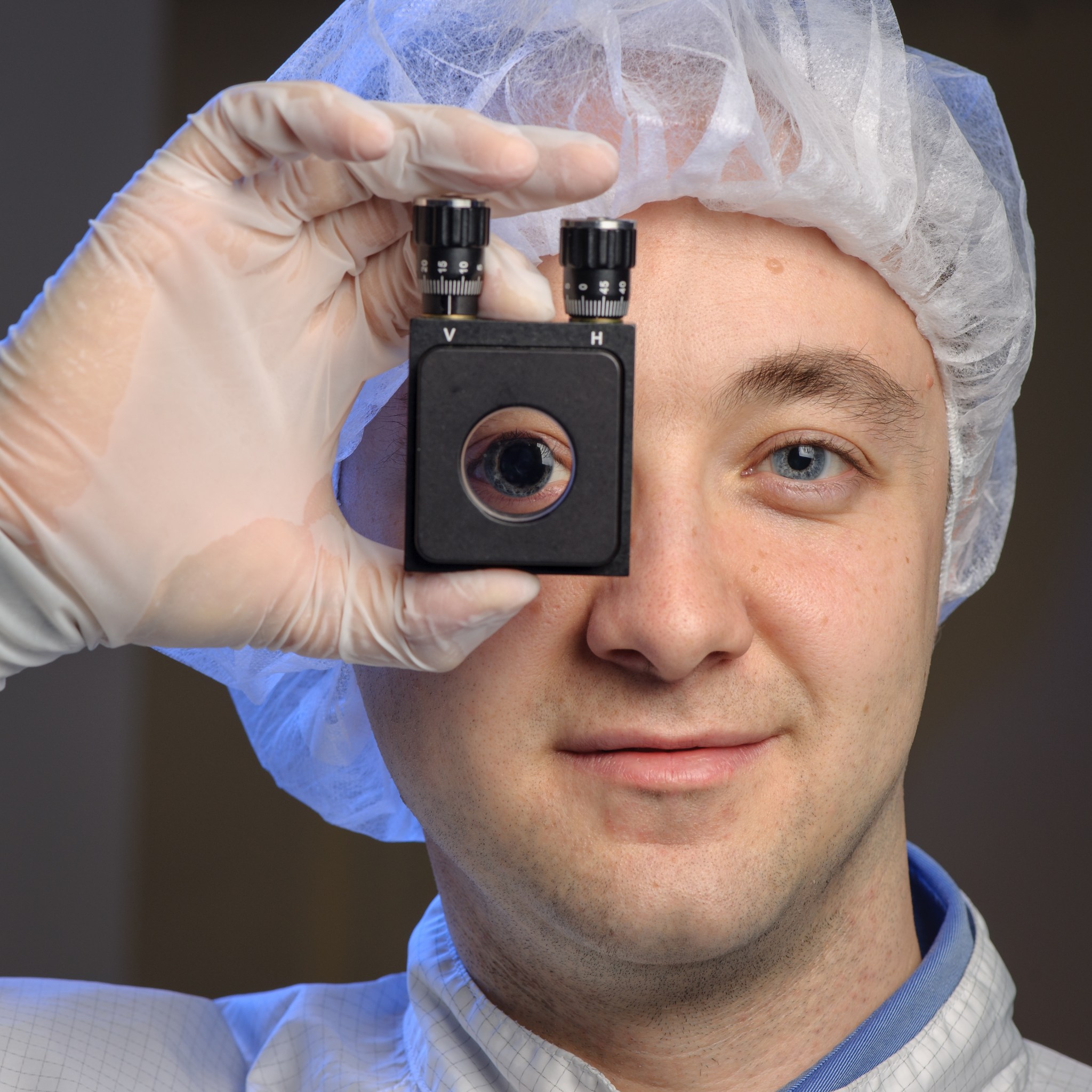 A man holding up a device to his eye, wearing gloves and a hairnet.