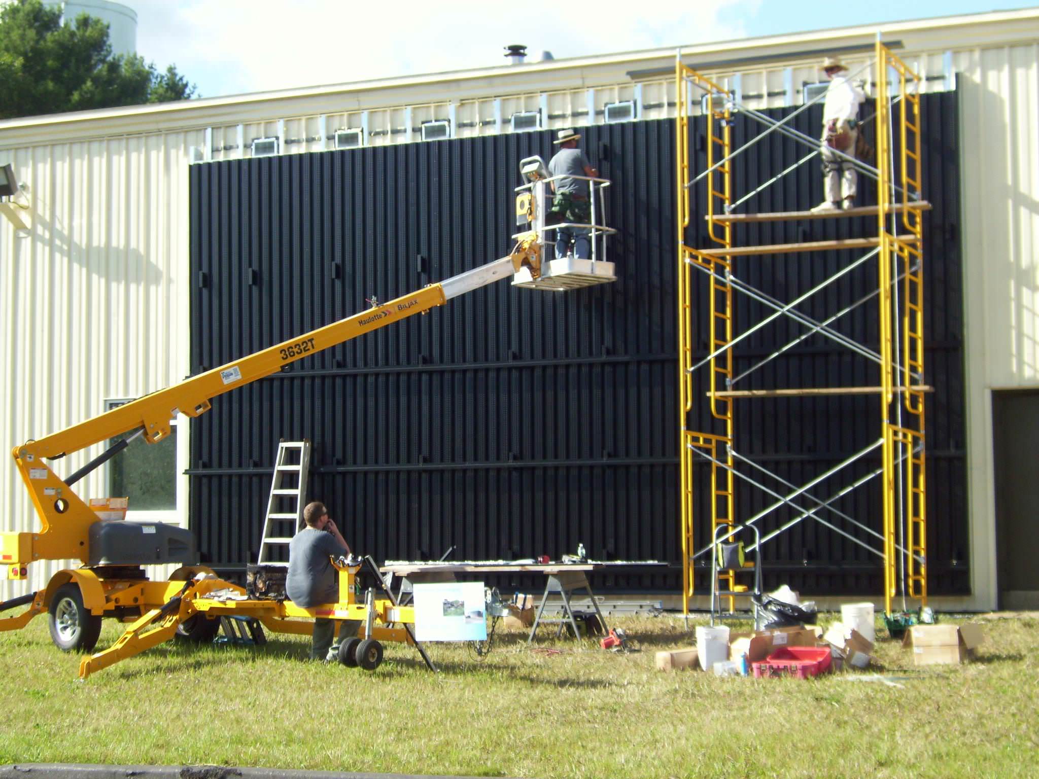 workers installing a solar wall at the Wicked Joe coffee company, there's a crane and rafters against a building lined with solar panels