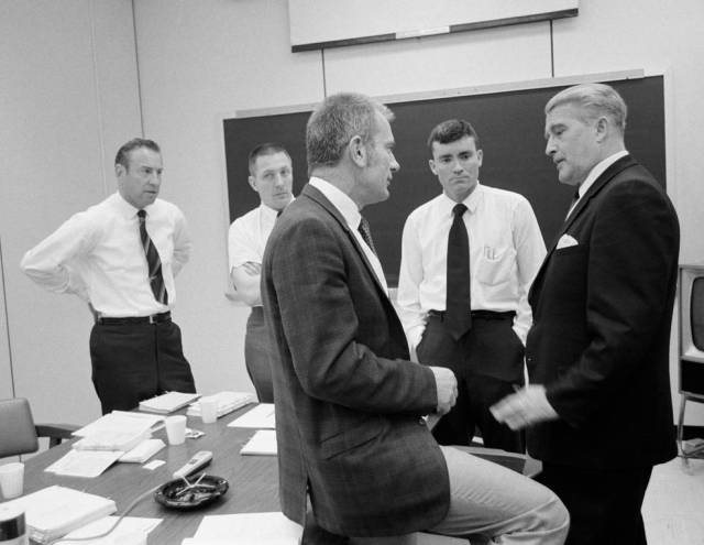 Dr. Donald K. Slayton (center foreground), Manned Spaceflight Center director of flight crew operations, talks with Dr. Wernher von Braun (right), at an Apollo 13 postflight debriefing session on April 20, 1970. The three crewmen of the Apollo 13 mission (left to right) in the background are astronauts James A. Lovell, Jr., commander; John L. Swigert Jr., command module pilot; and Fred W. Haise Jr., lunar module pilot.