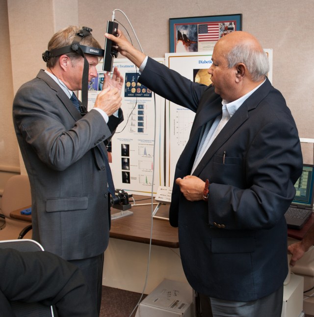 A NASA researcher demonstrates an optical measuring device on a man wearing hardware strapped to his head.