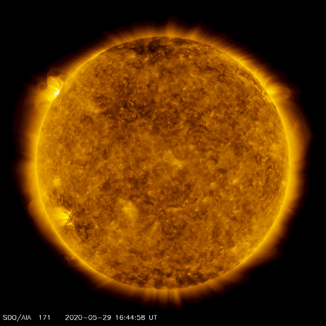 A satellite image of the Sun, colorized in gold. A bright spot of light hovers over the left horizon.