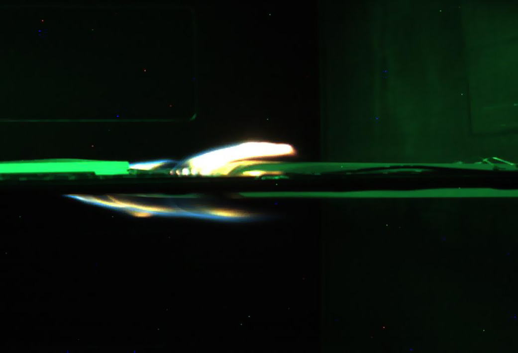 A blue flame burns from side to side in a microgravity fire experiment.