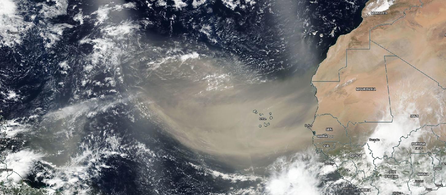 Satellite image of a large light brown plume of Saharan dust over the westernmost part of northern Africa and over the Atlantic ocean. Clouds are speckled across the image. 