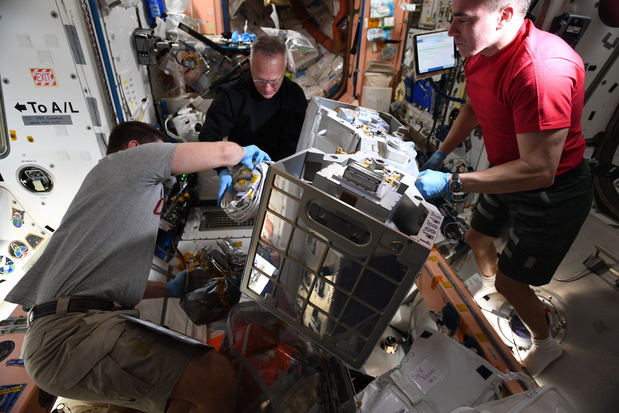 Astronauts Robert Behnken, Doug Hurley, and Chris Cassidy aboard ISS, working on a gray piece of technology together.
