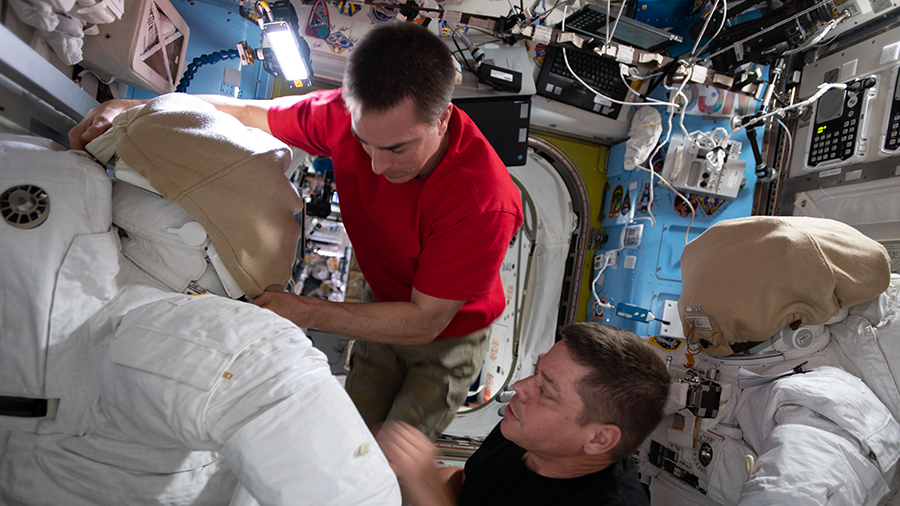 NASA astronauts (from top) Chris Cassidy and Bob Behnken work on U.S. spacesuits inside the International Space Stationâs Quest airlock.