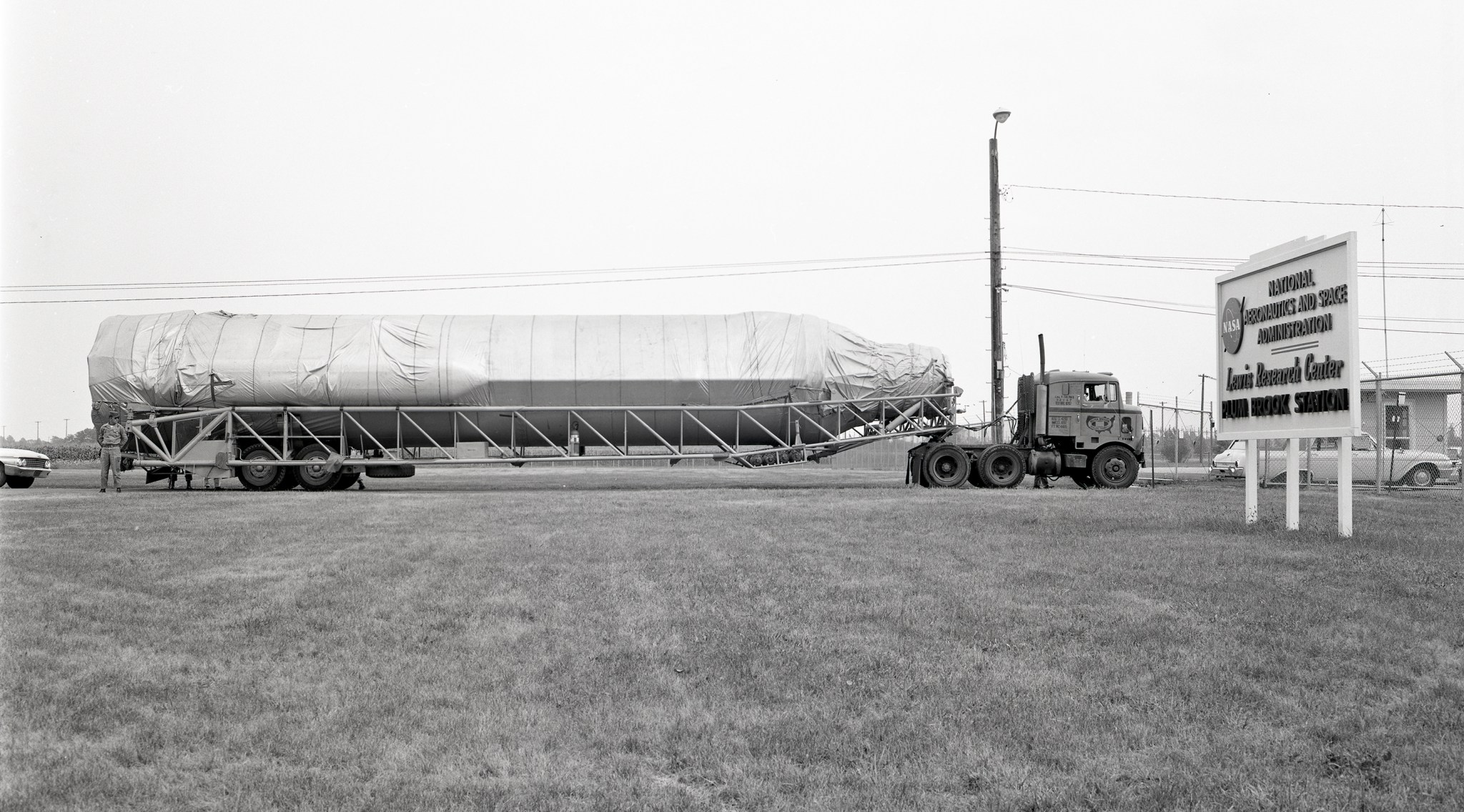 A rocket sits horizontally on a flatbed tractor trailer outside front gate.