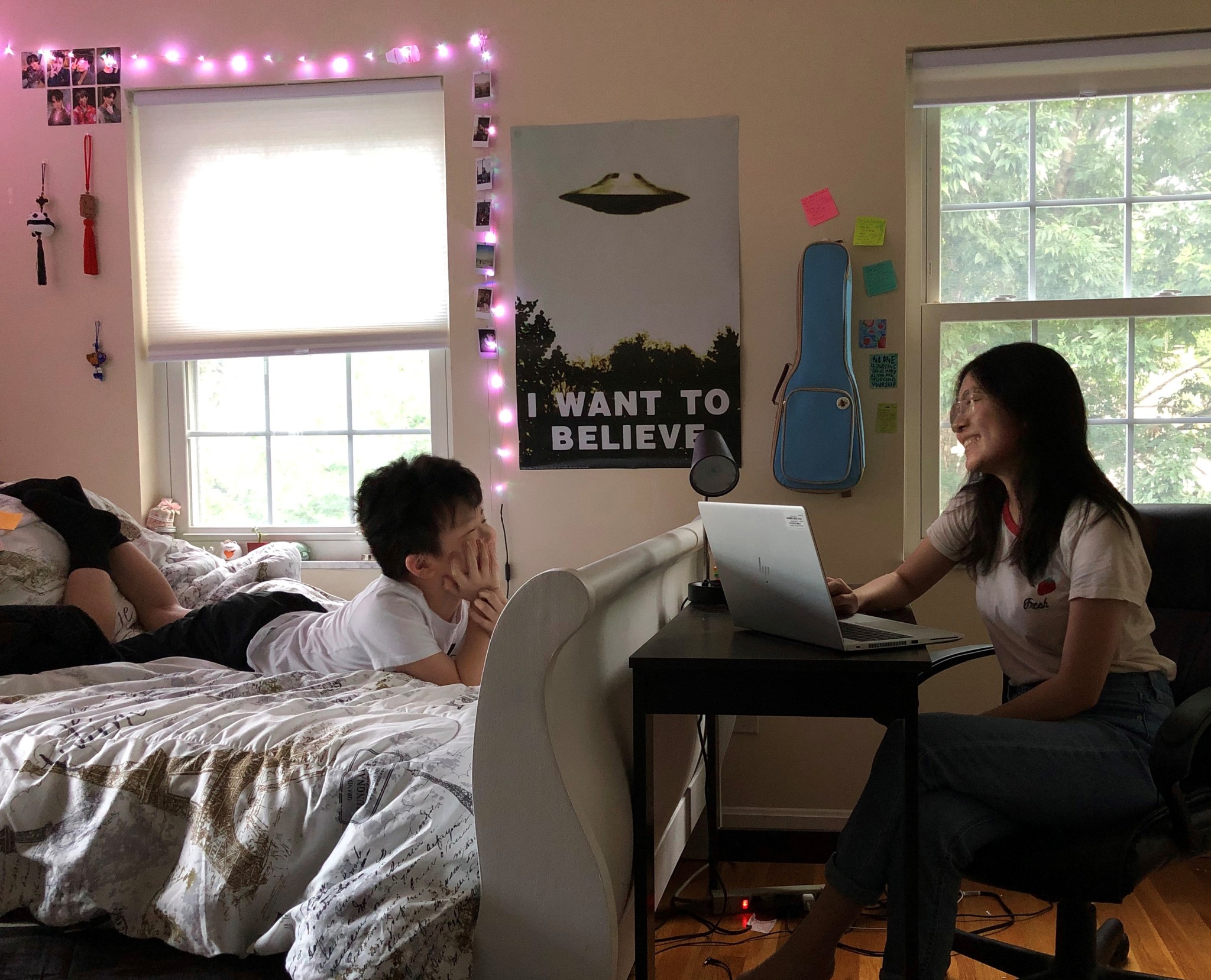 College student laughs with her young brother as she works at a desk with a computer.