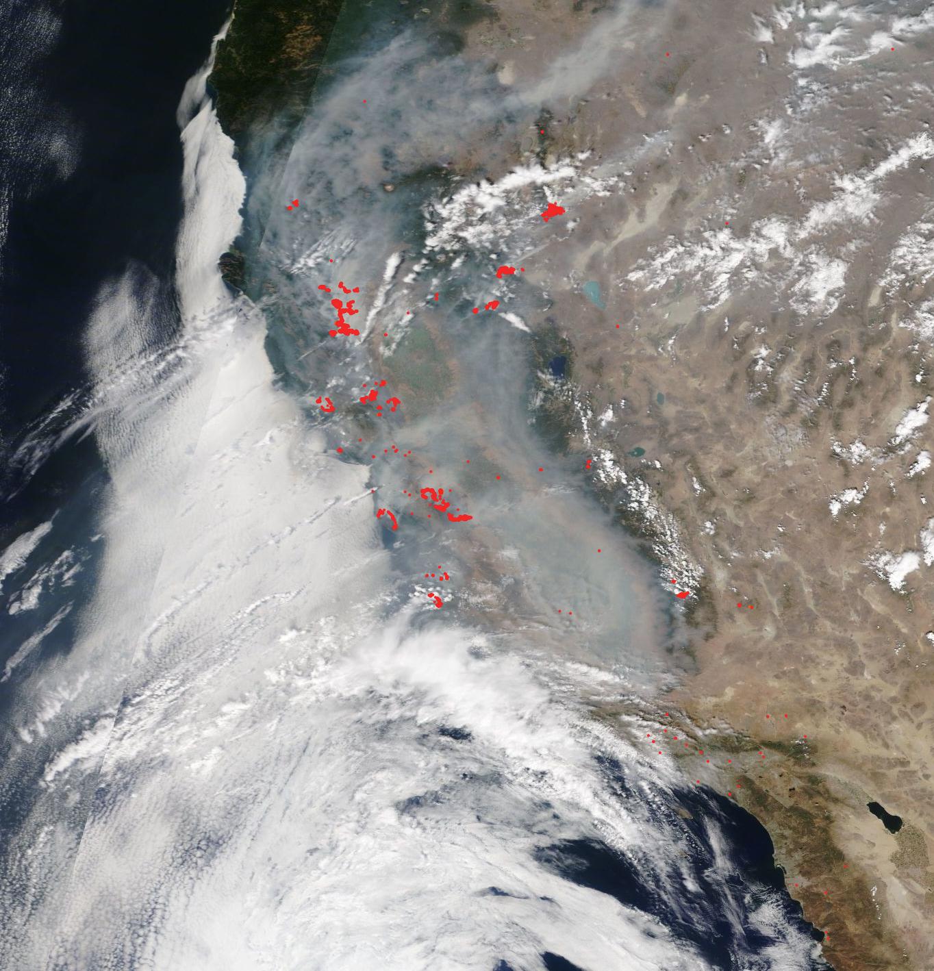 Satellite image of coast of California with a large amount of white smoke covering the left half of the image over the ocean and land. On the right, tan land is visible. 