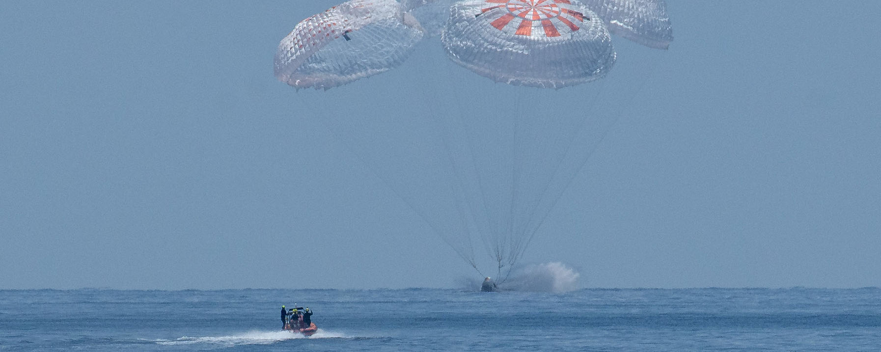 Capsule splashing down in ocean with boat approaching it