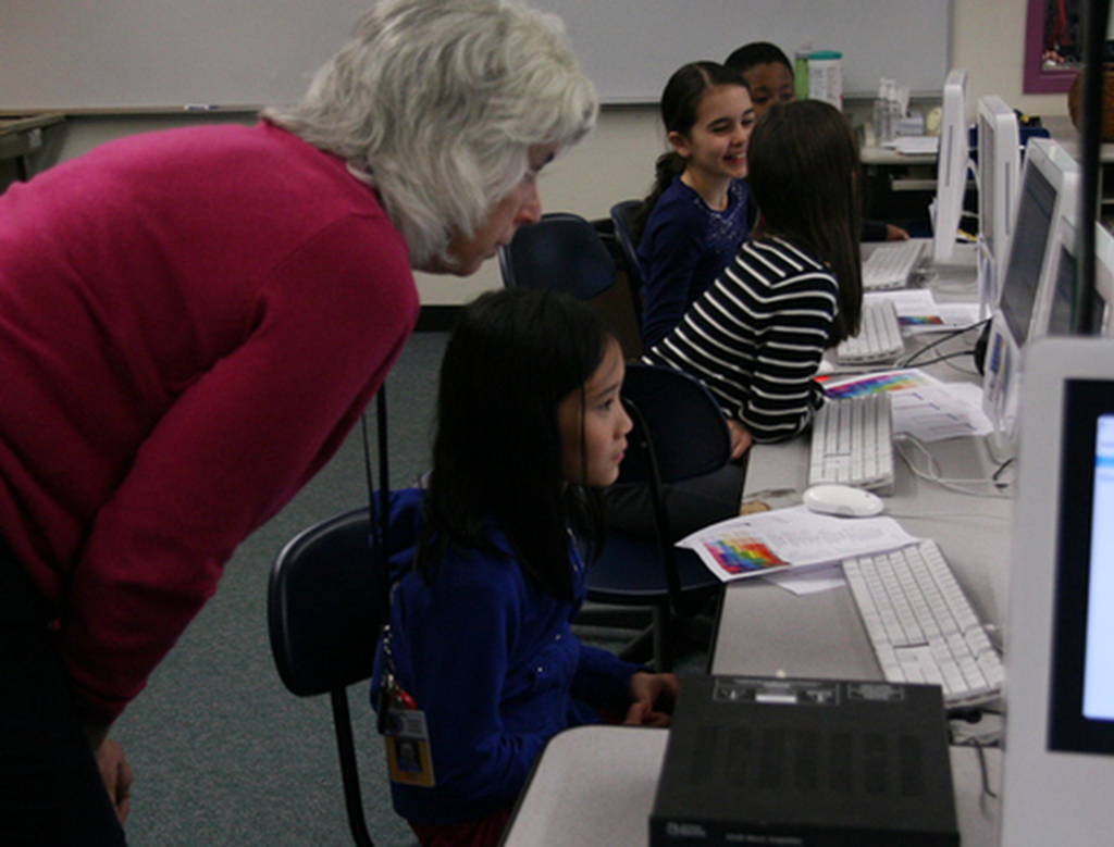 Young girl works at computer station while a teacher looks on