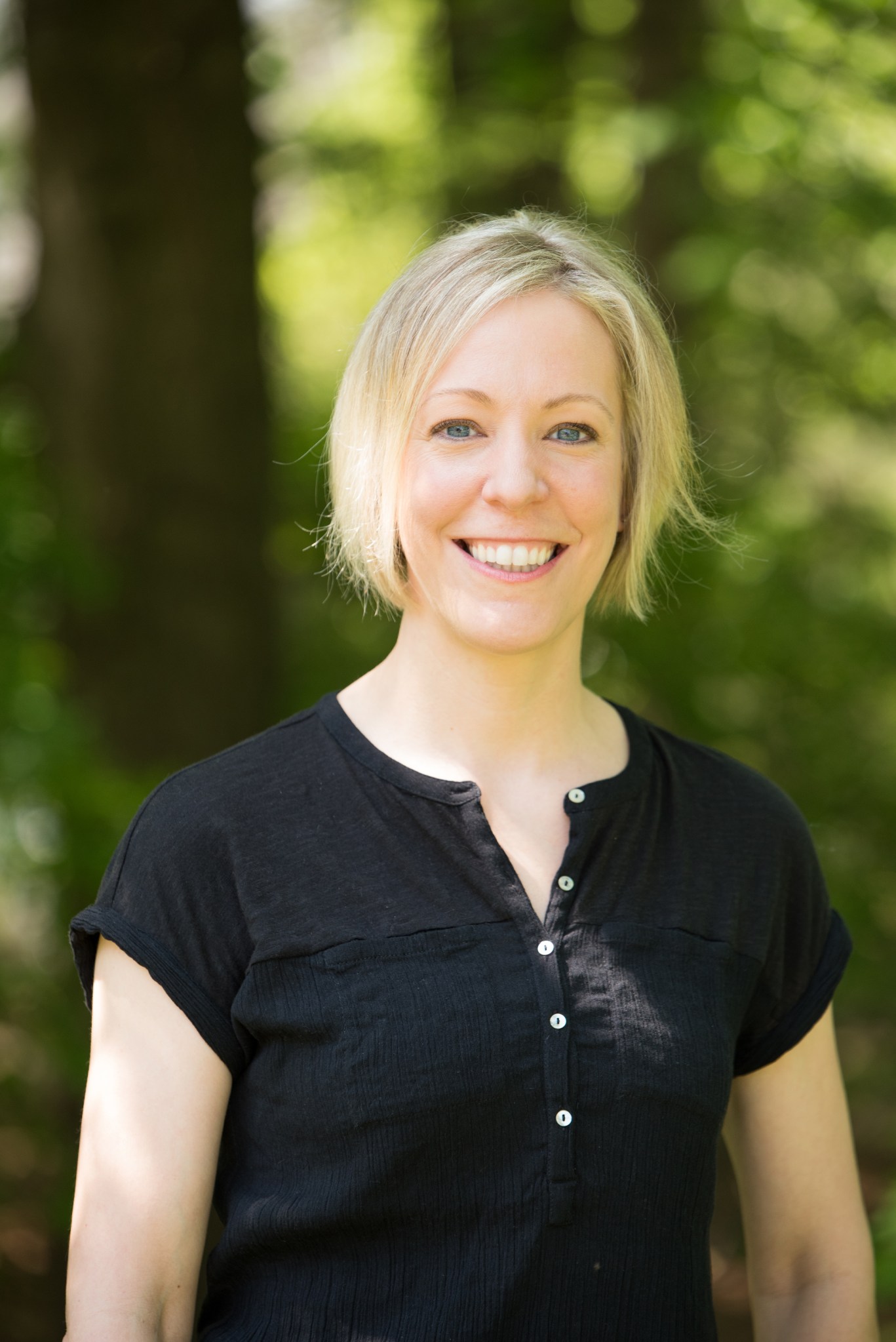 Woman with short, blonde hair wears a black t-shirt and smiles outside.