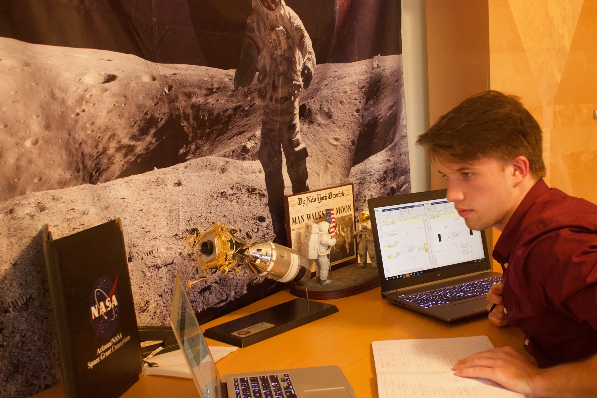 A college student looks at his computer while surrounded by NASA memorabilia.