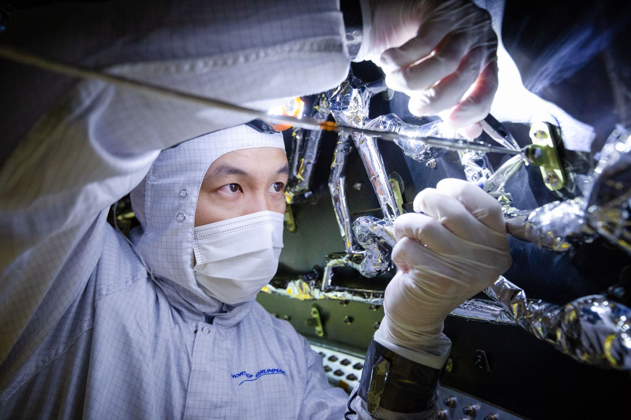 white bunny suit-clad Webb technician in clean room using tools