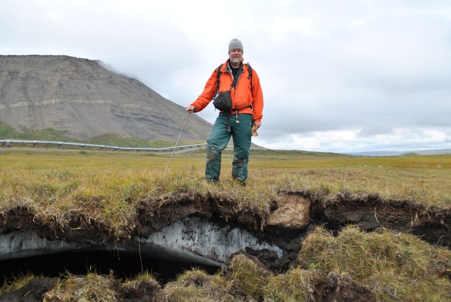 Kevin Schaefer standing above melting ground ice in front of the Alaska pipeline on the North Slope.