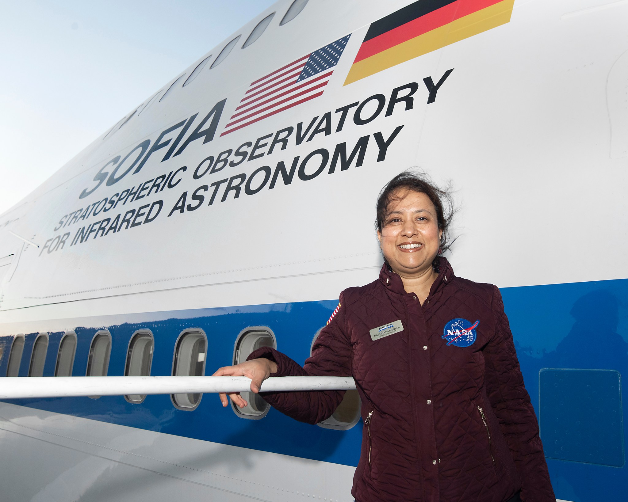 Woman (Naseem) standing next to SOFIA with the words Stratospheric Observatory for Infrared Astronomy behind her.